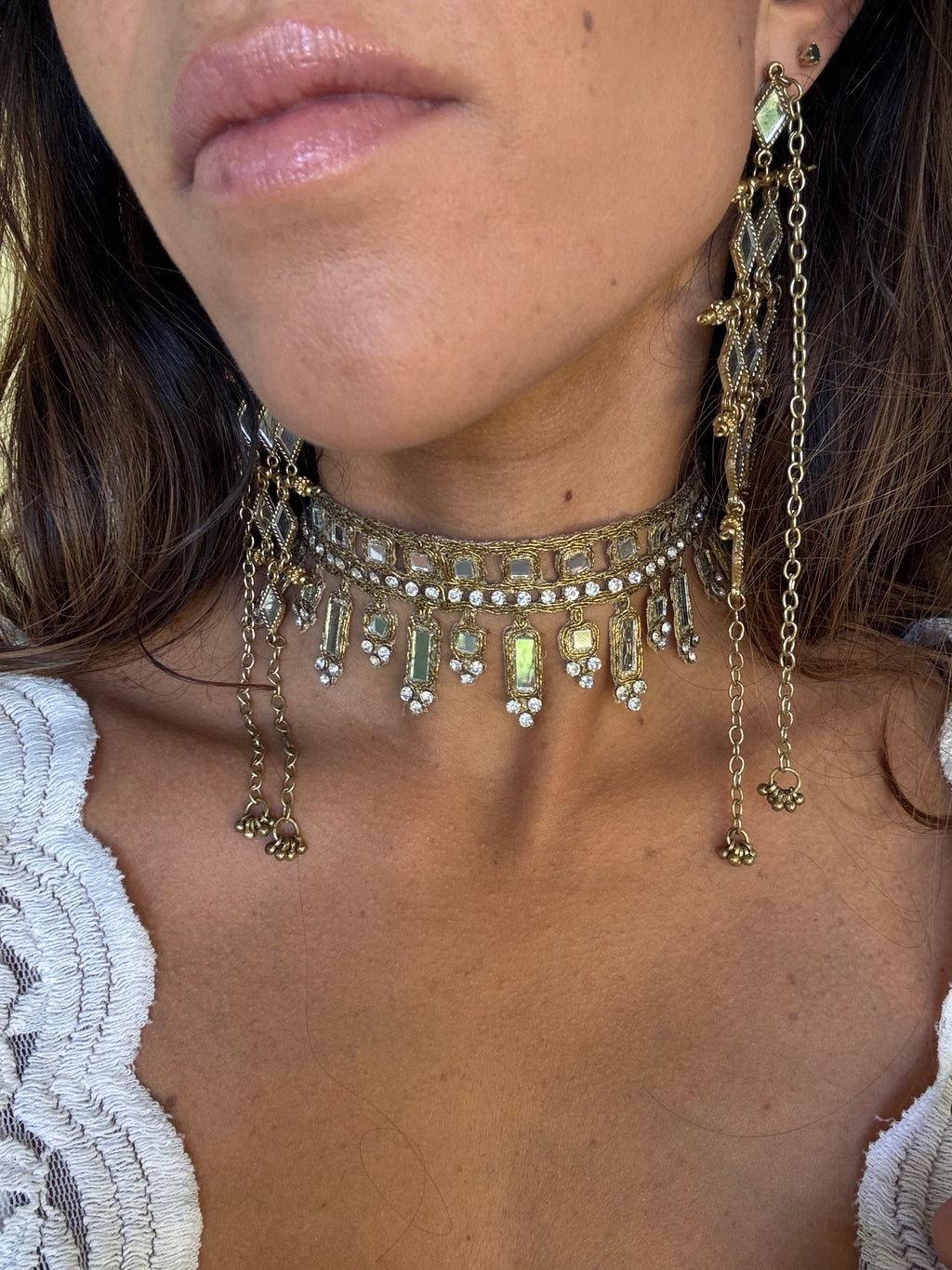 Close-up of a person wearing gold jewelry with gemstones on their neck and chest.