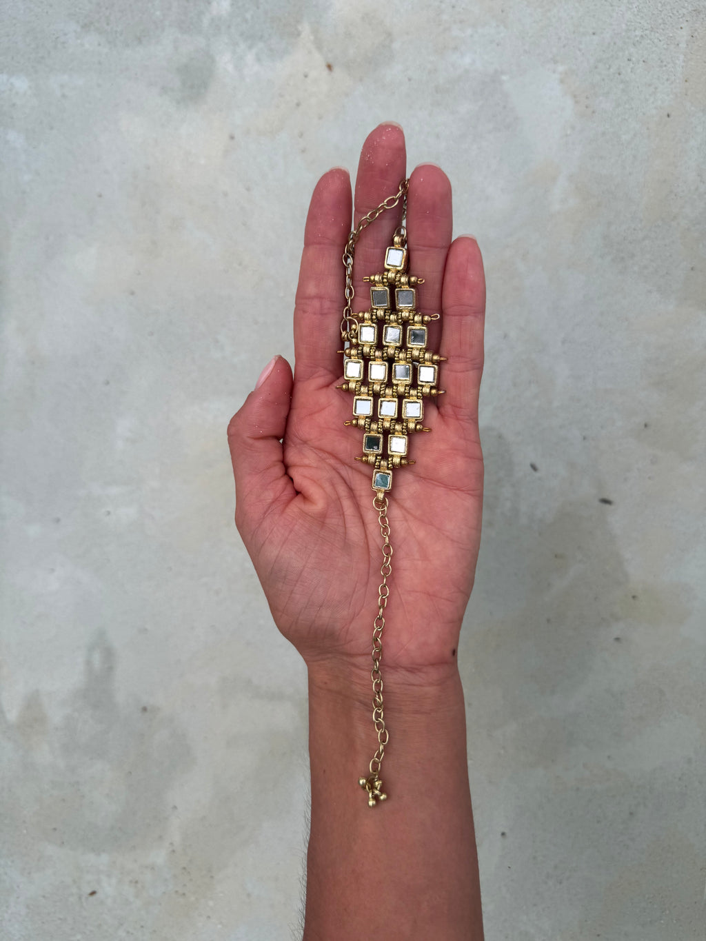 Hand holding a gold necklace with embedded stones on a light background