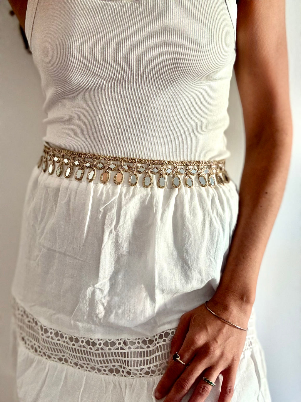 White sleeveless top with a decorative belt and lace hem on a plain background