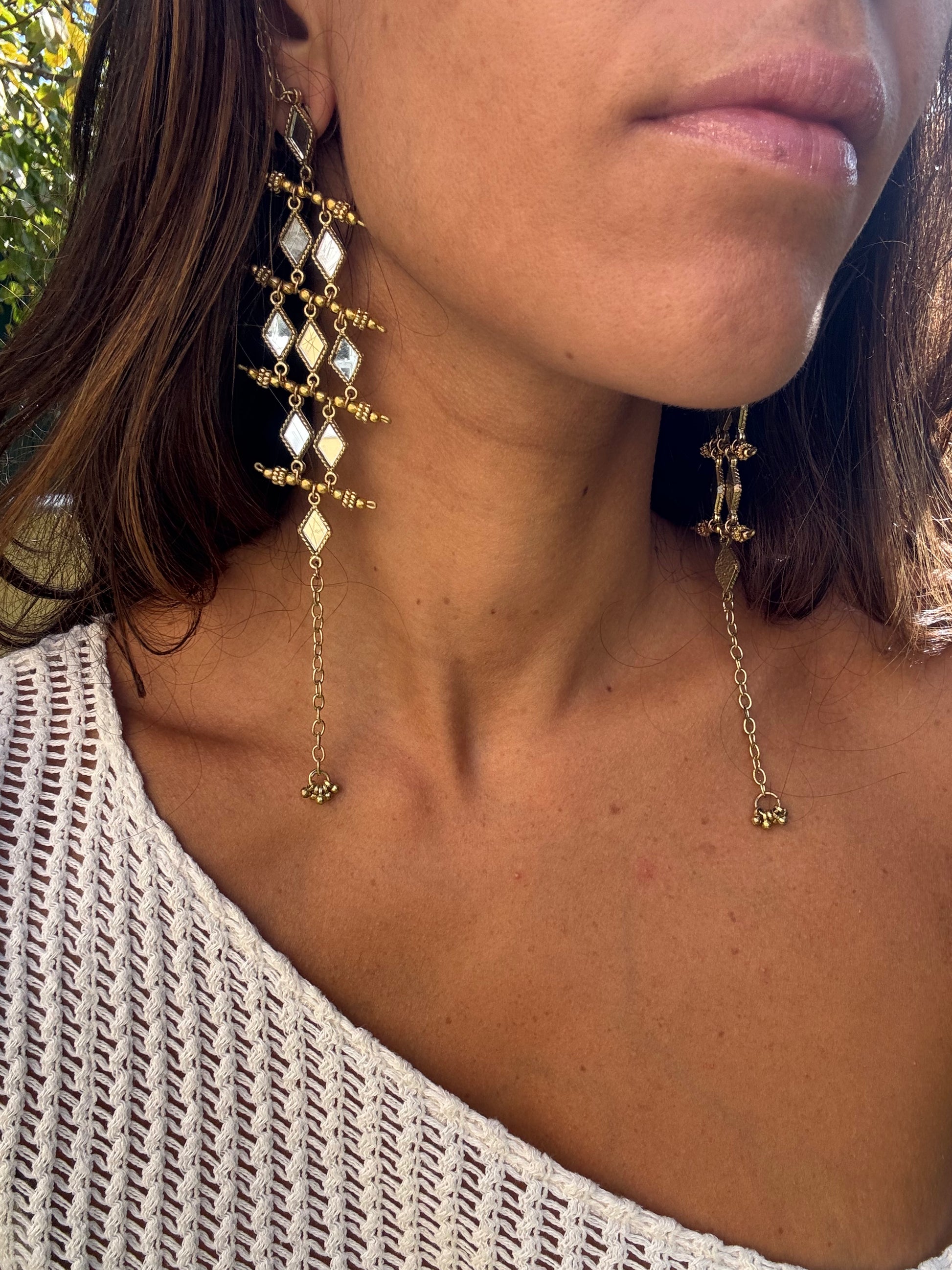 Close-up of a person wearing gold earrings with dangling chains.
