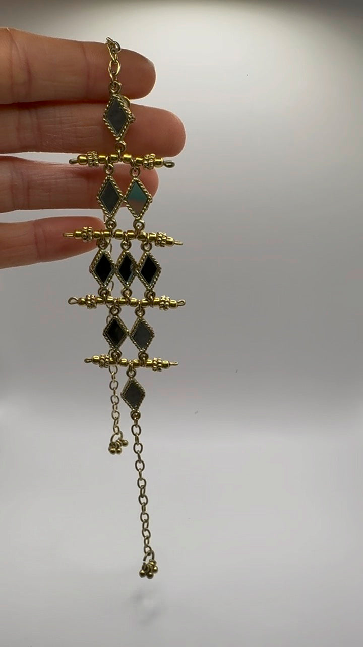 Gold and black decorative earring held by a hand against a plain background