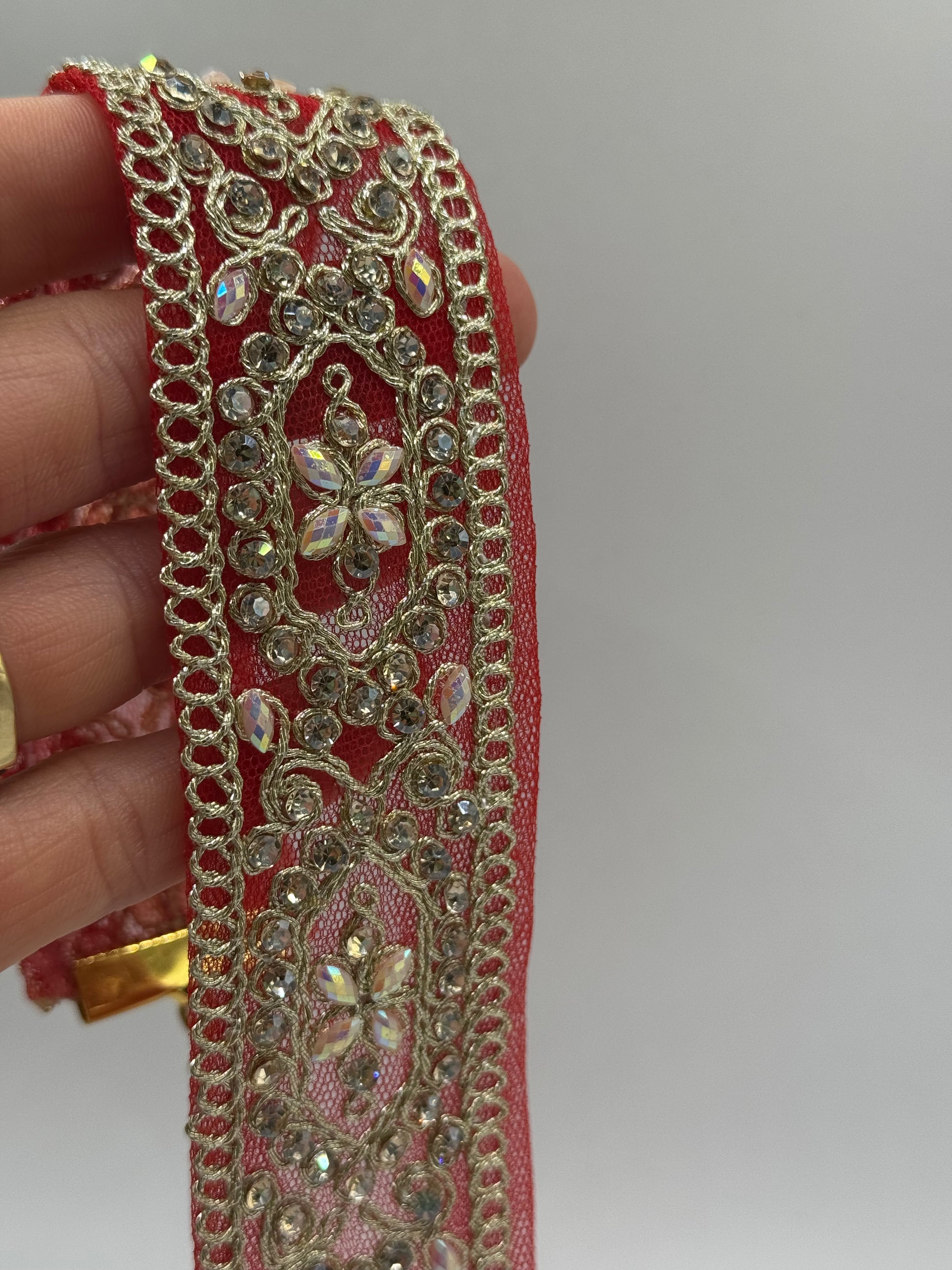 Decorative red and gold ribbon with intricate patterns held by a hand against a neutral background