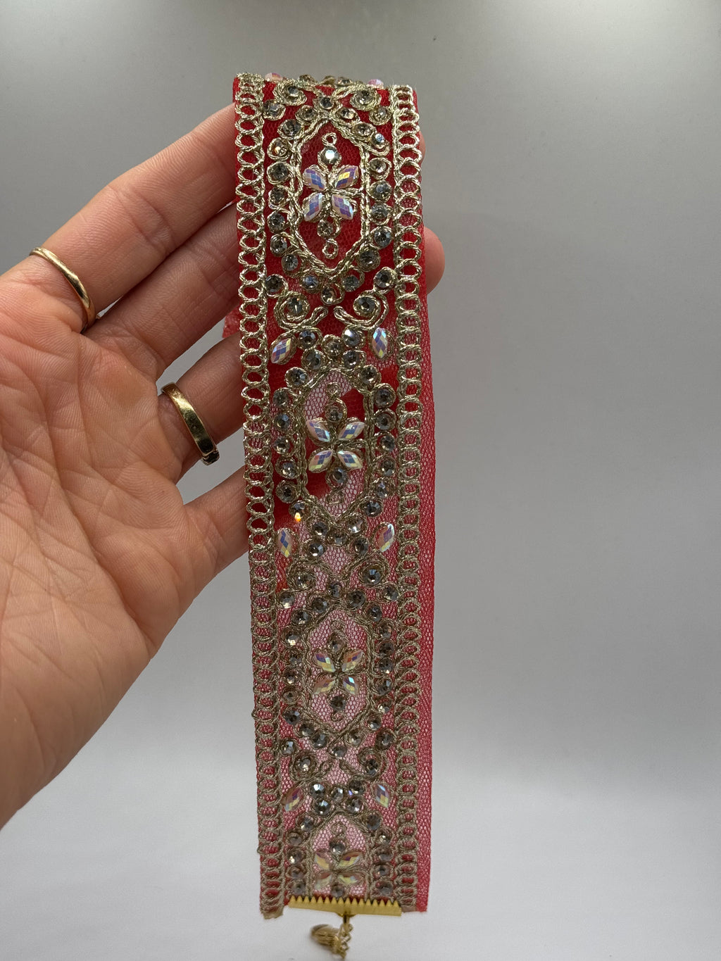 Decorative red and gold bracelet held by a hand on a plain background