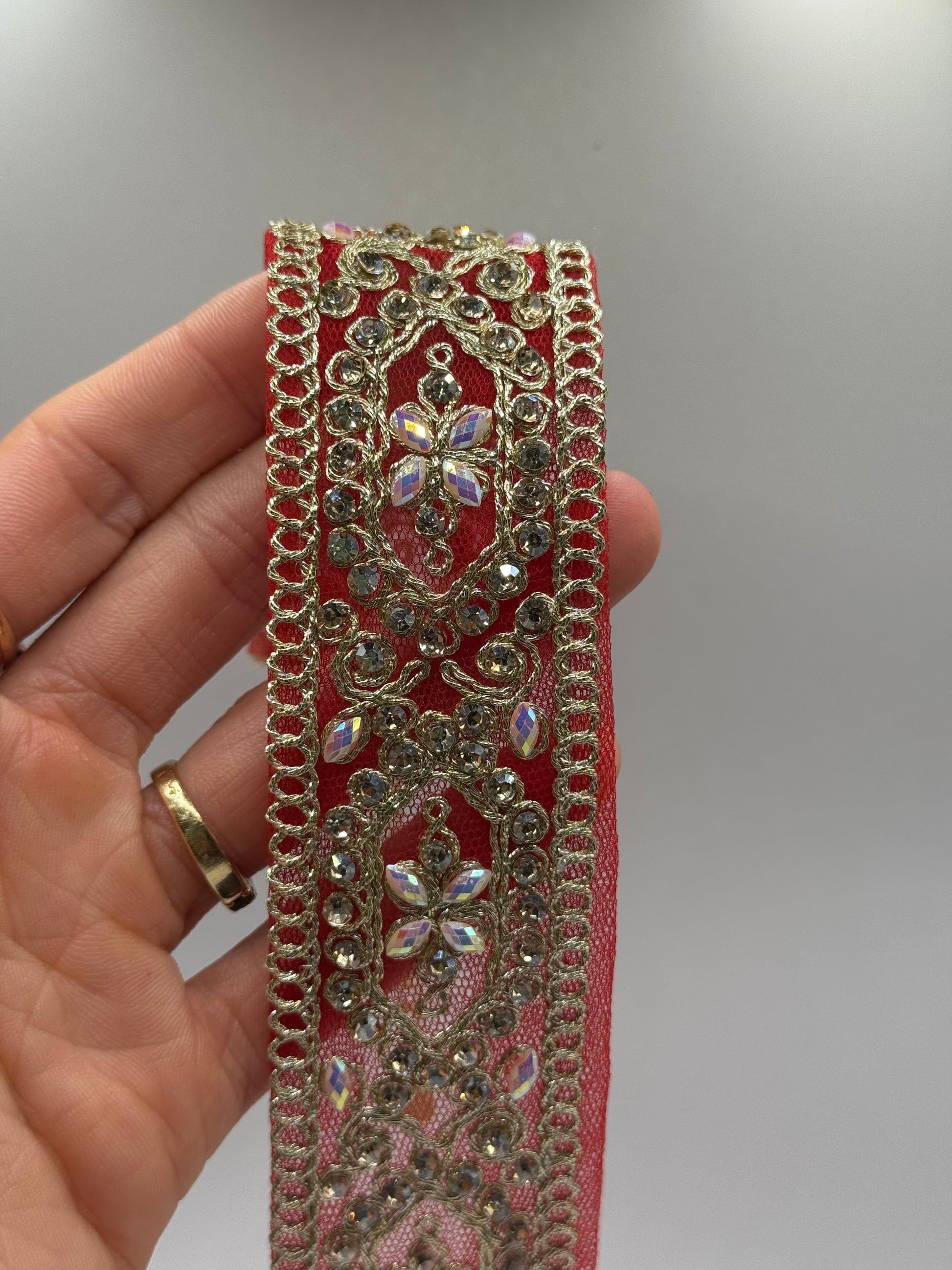 Decorative red ribbon with gold embellishments held by a hand against a neutral background