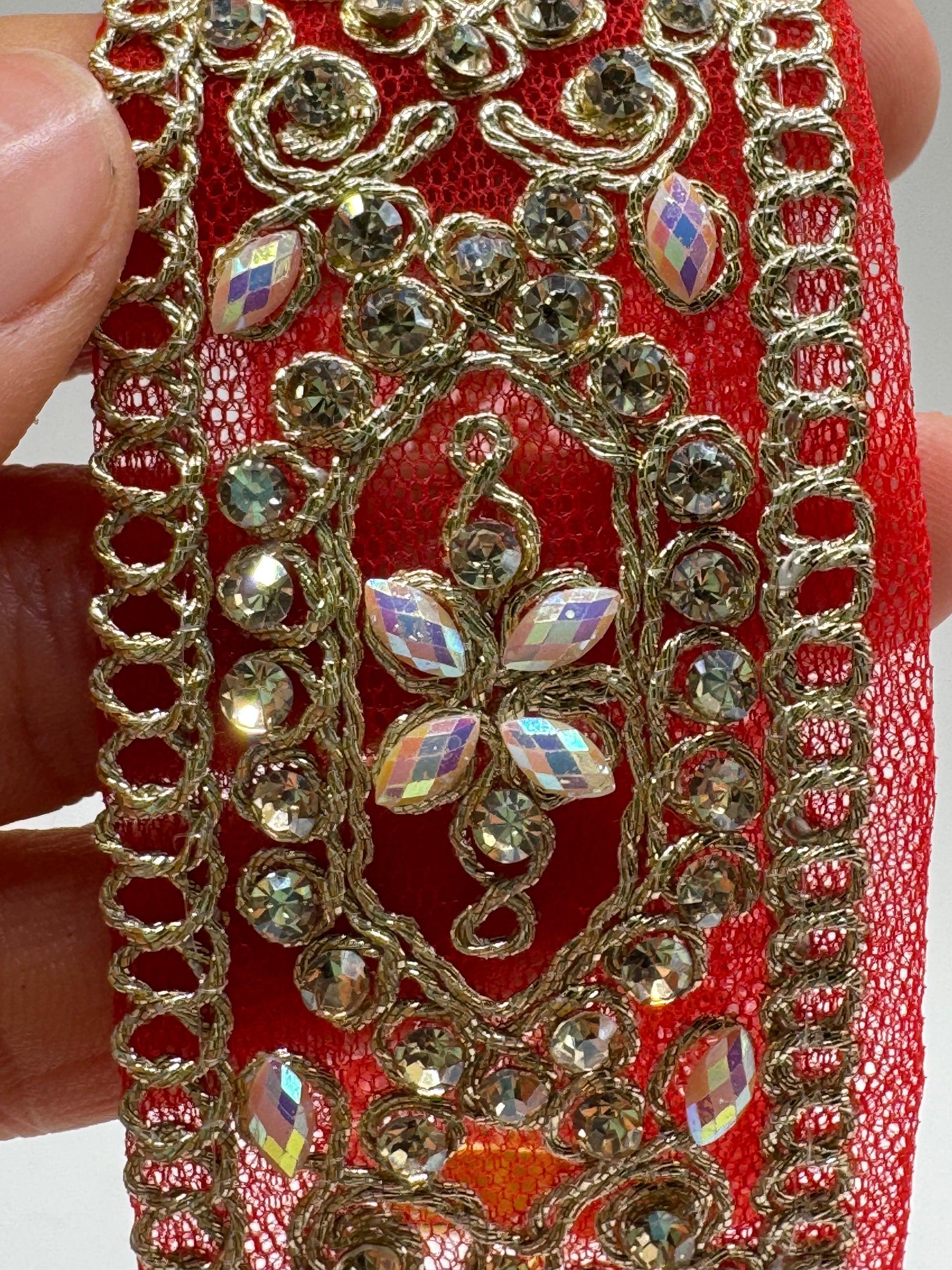 Decorative red fabric with gold embroidery and embellishments held by a hand.