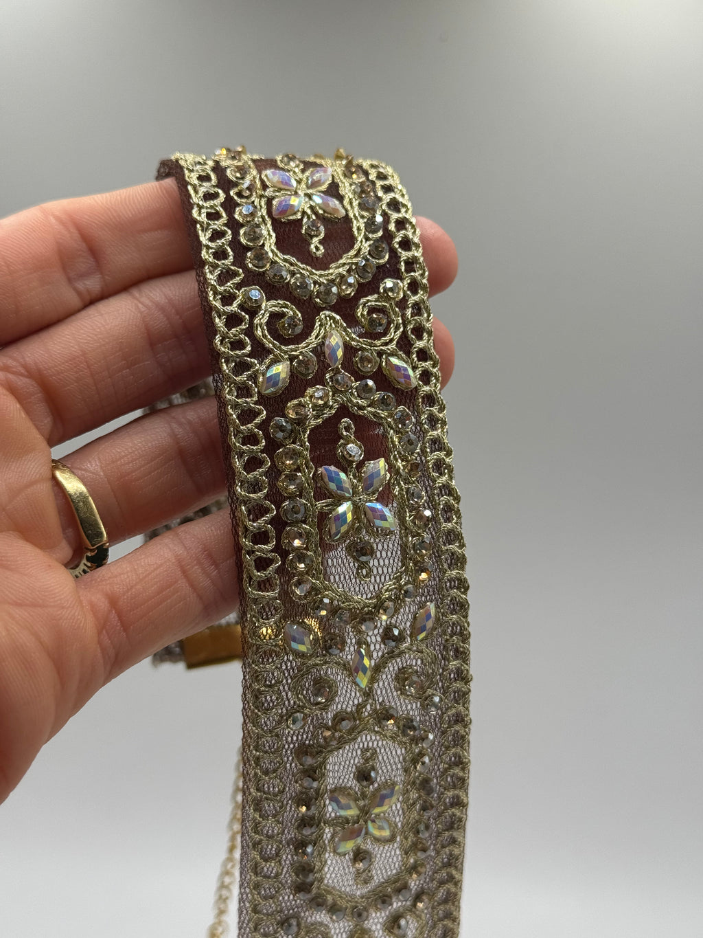 Decorative lace trim held by a hand with a gold ring on a plain background