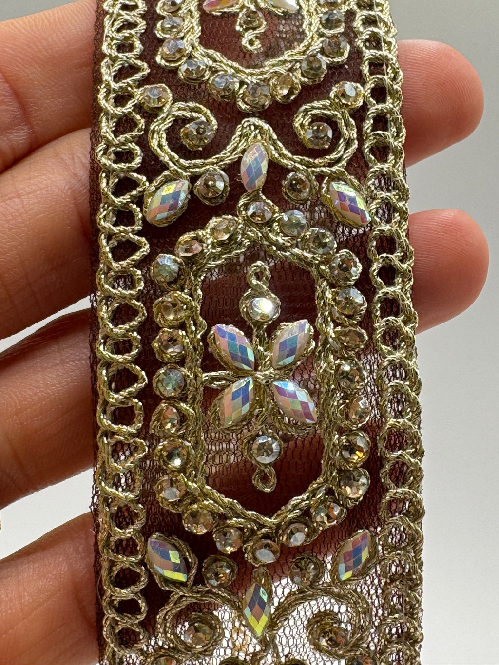 Decorative lace trim with rhinestones held between fingers against a neutral background