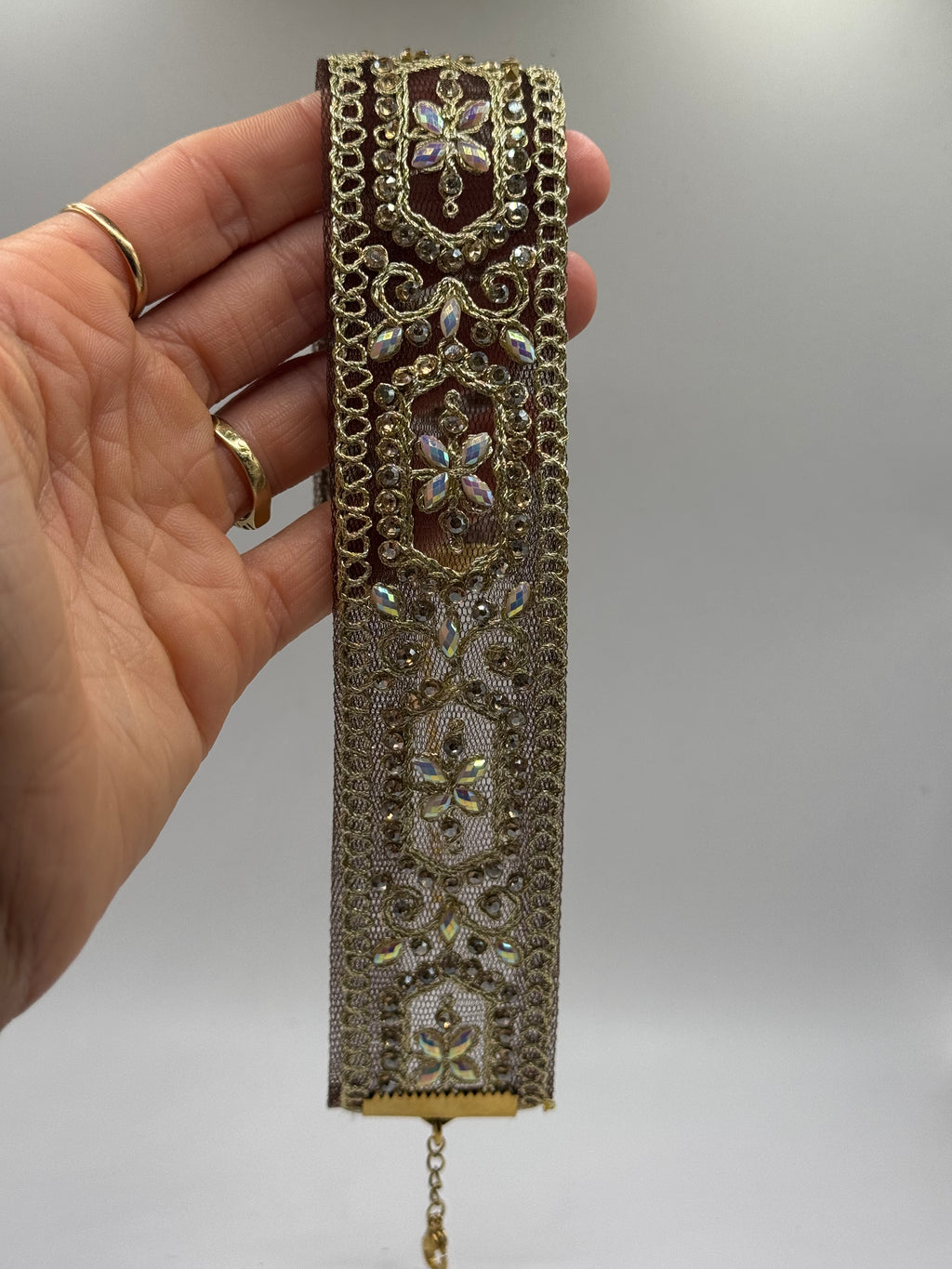 Decorative belt with intricate patterns held by a hand against a neutral background