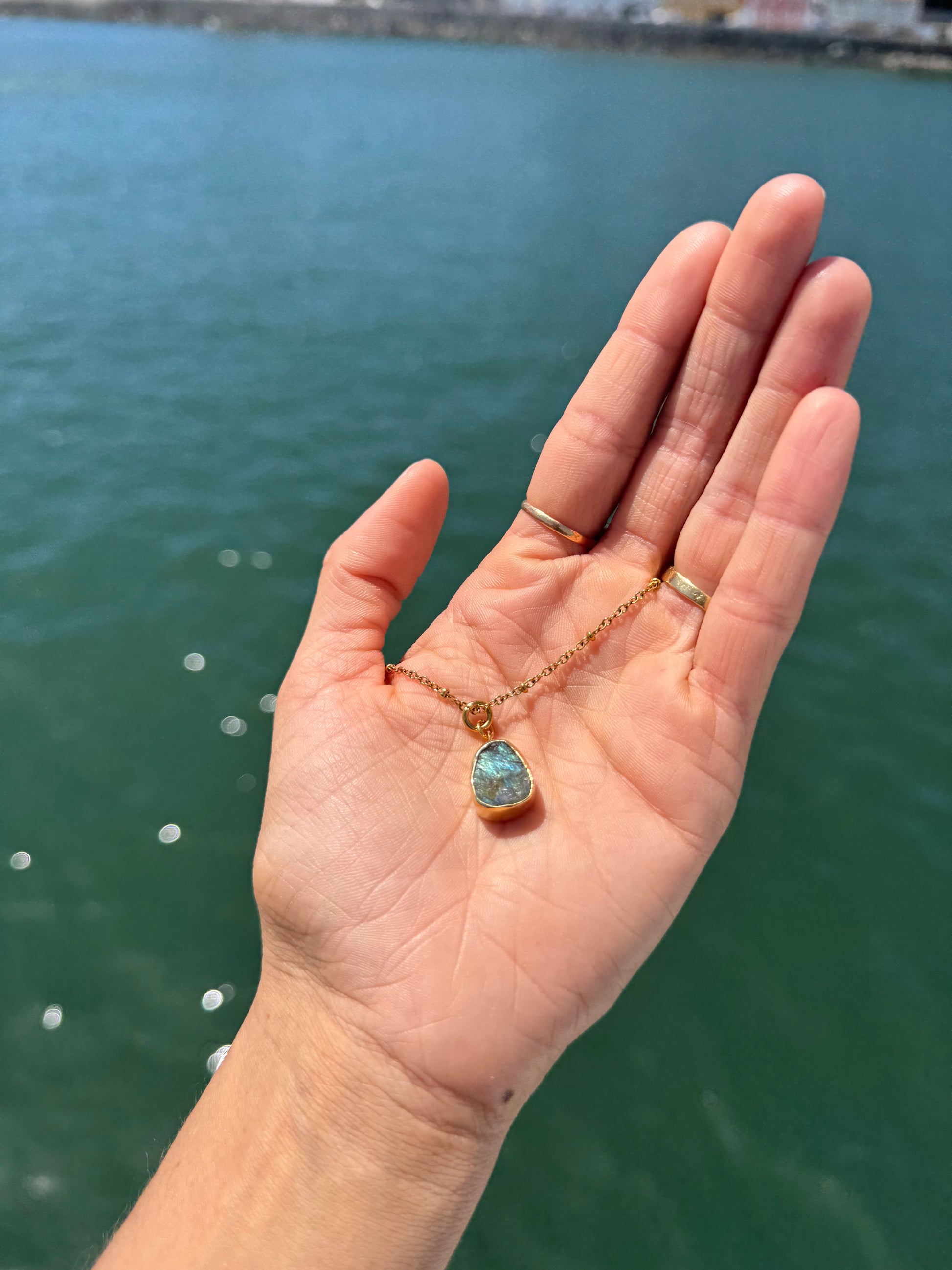 Hand holding a necklace with a blue pendant against a water background