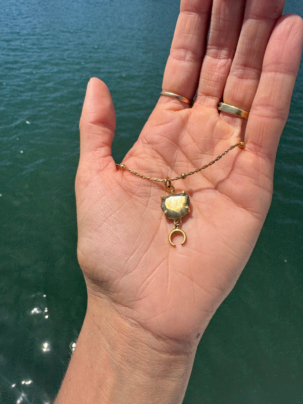 Hand holding a necklace with a pendant against a body of water