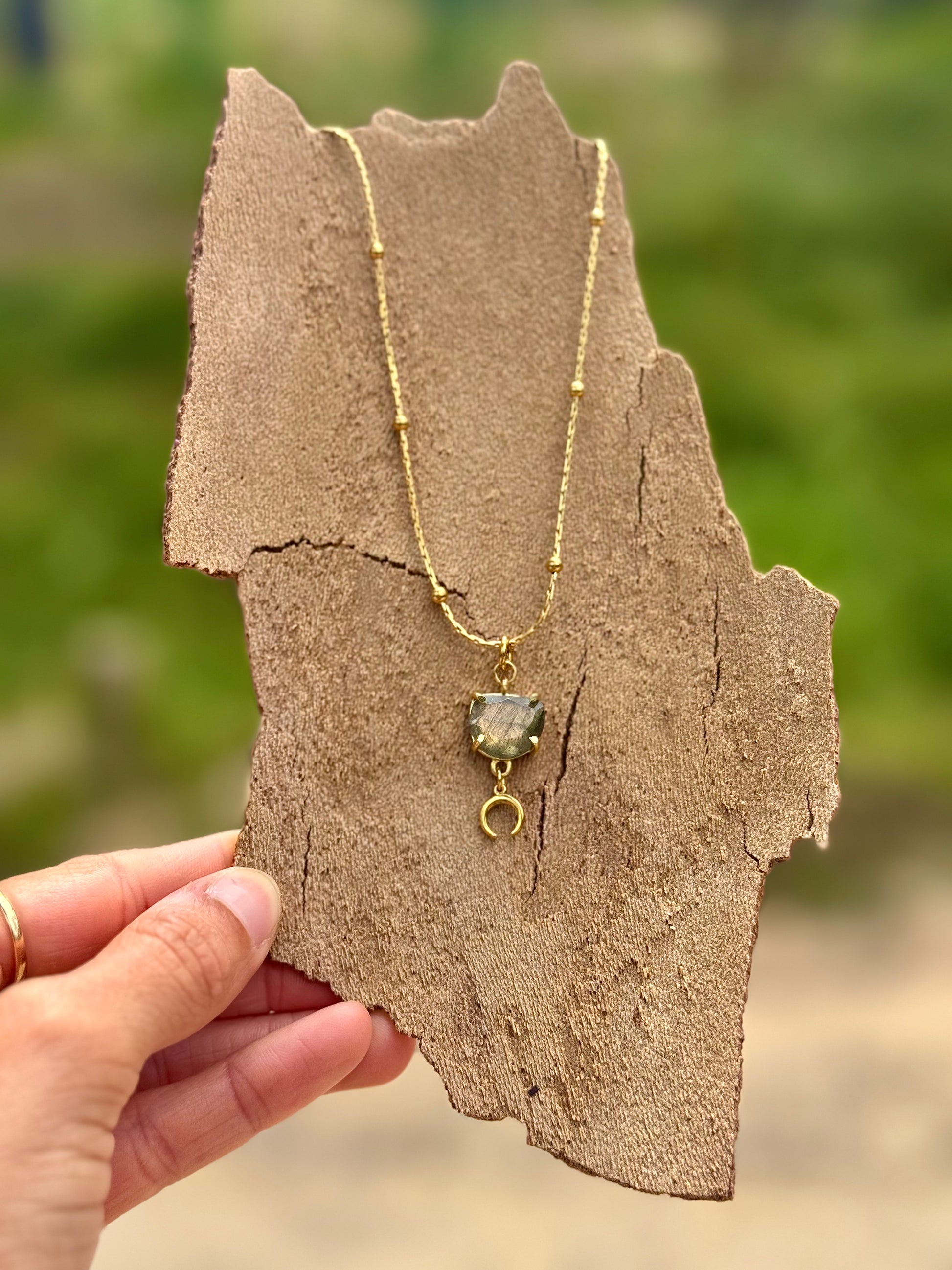 Gold necklace with a pendant held on a piece of brown paper against a blurred green background