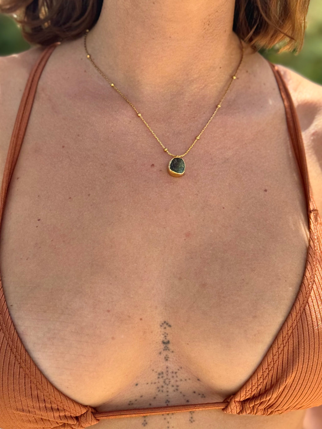 Person wearing a gold necklace with a green pendant, back view
