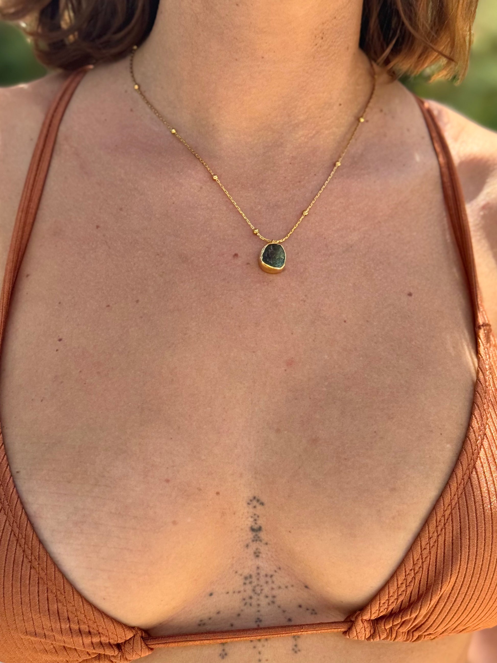 Person wearing a gold necklace with a green pendant, back view