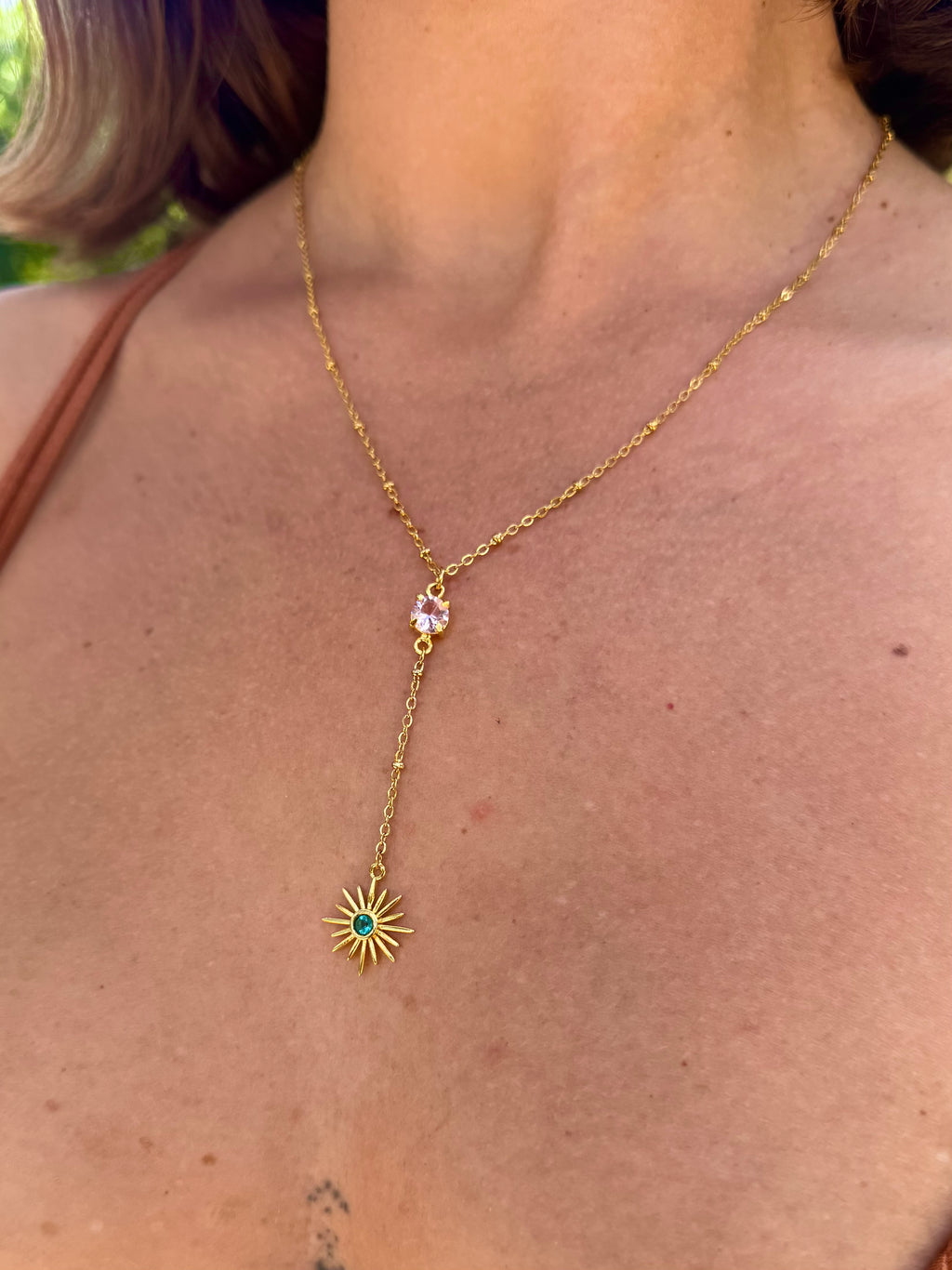 Gold necklace with a star-shaped pendant worn by a person outdoors