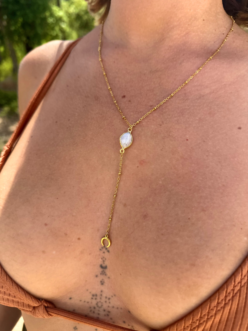 Gold necklace with a pendant on a person wearing a brown top outdoors.