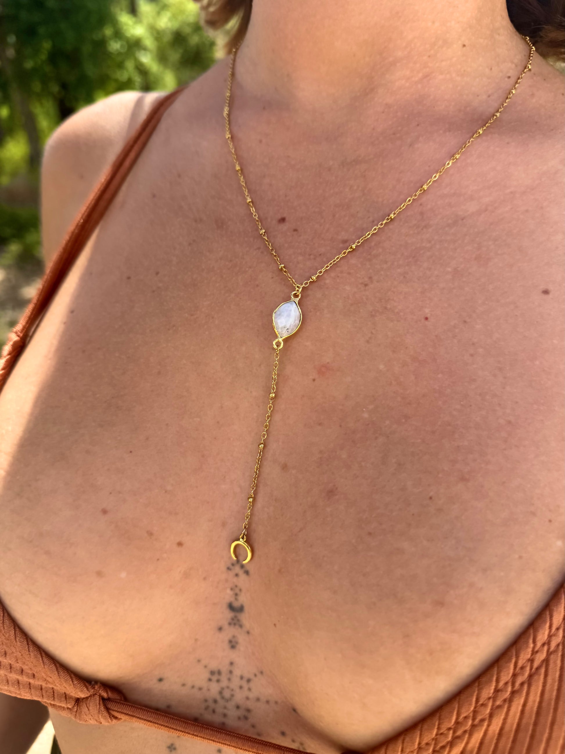 Gold necklace with a pendant on a person wearing a brown top outdoors.