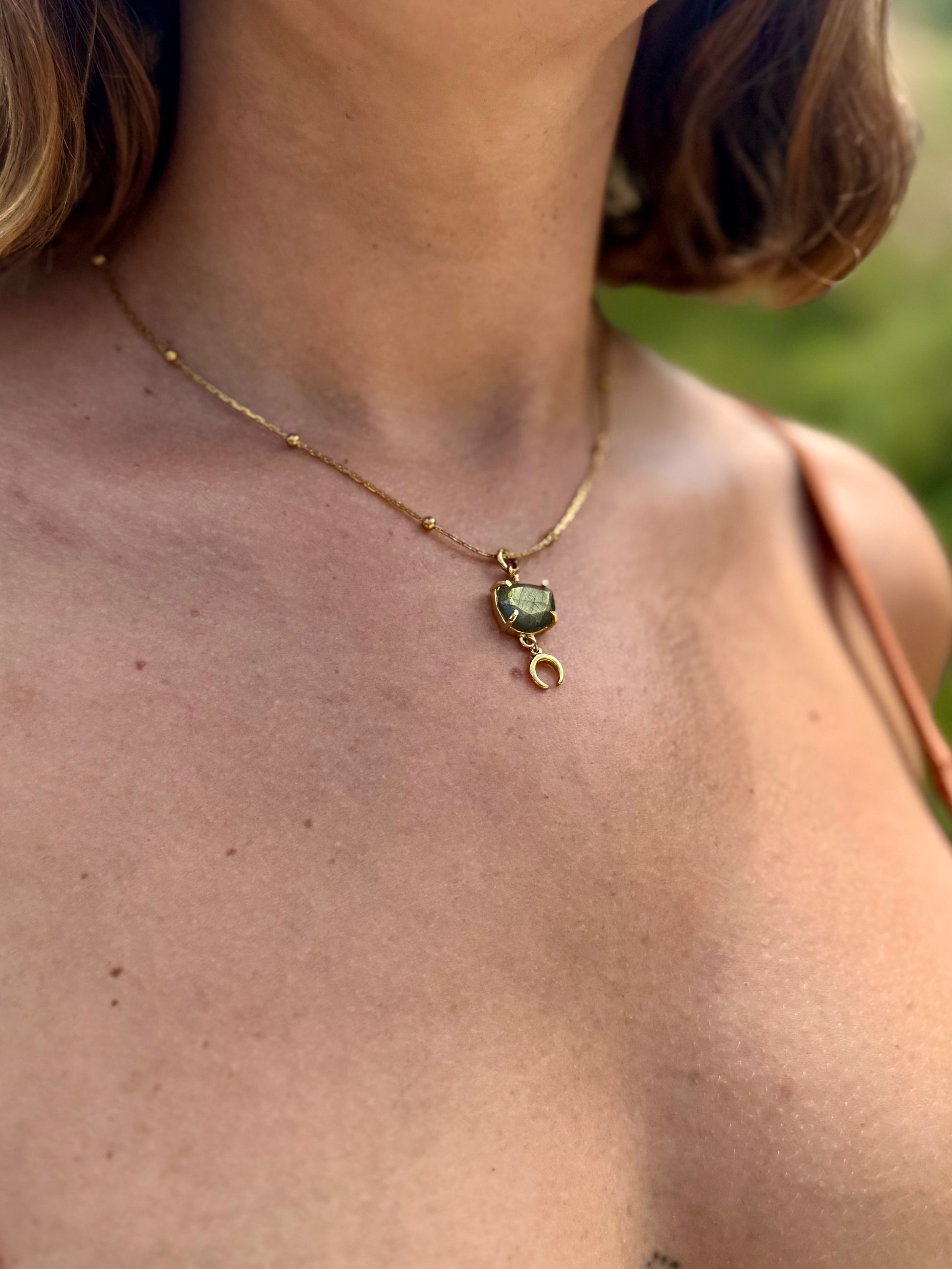 Close-up of a necklace with a green gemstone on a person's neck outdoors.