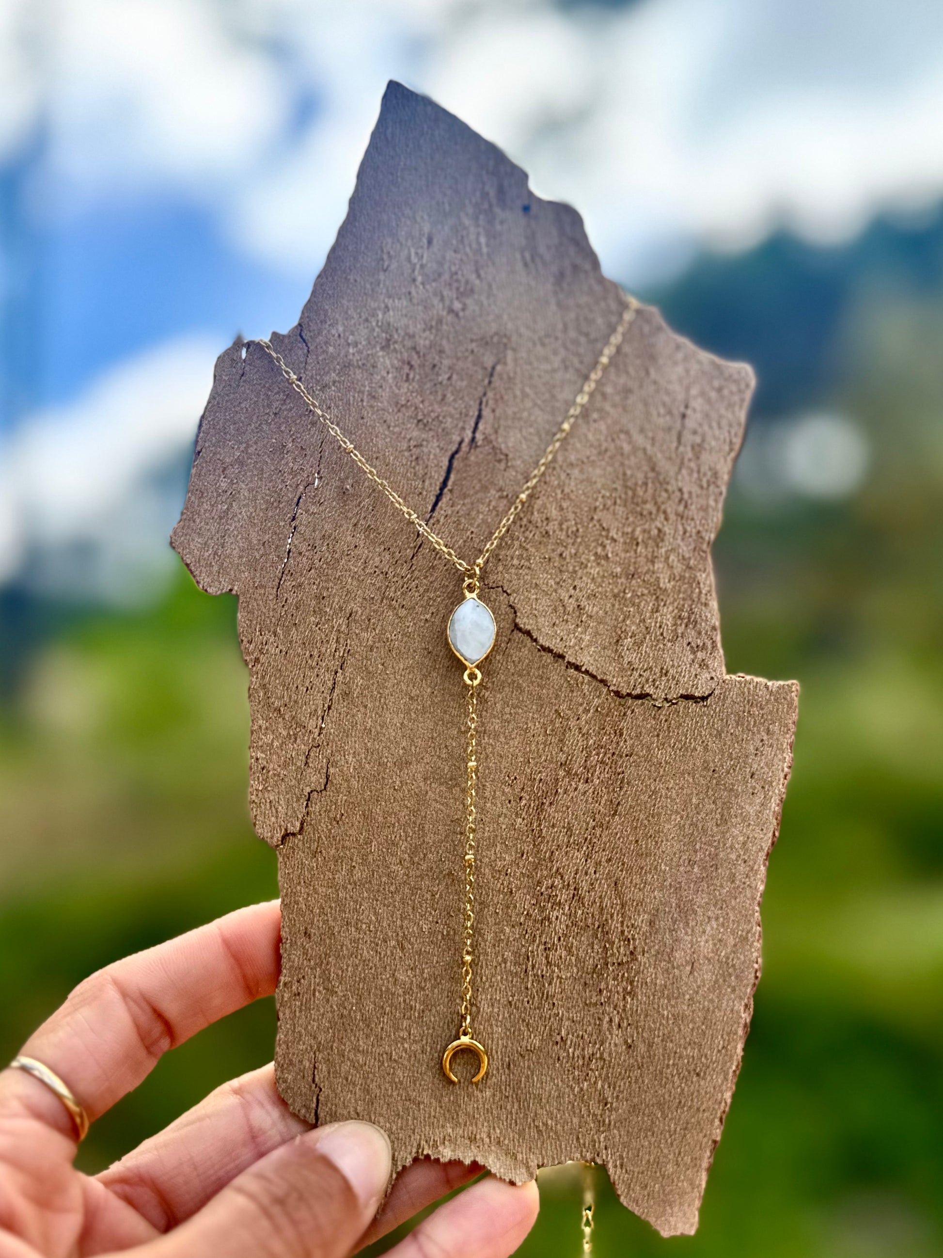 Gold necklace with a pendant held on a piece of brown paper against a blurred natural background