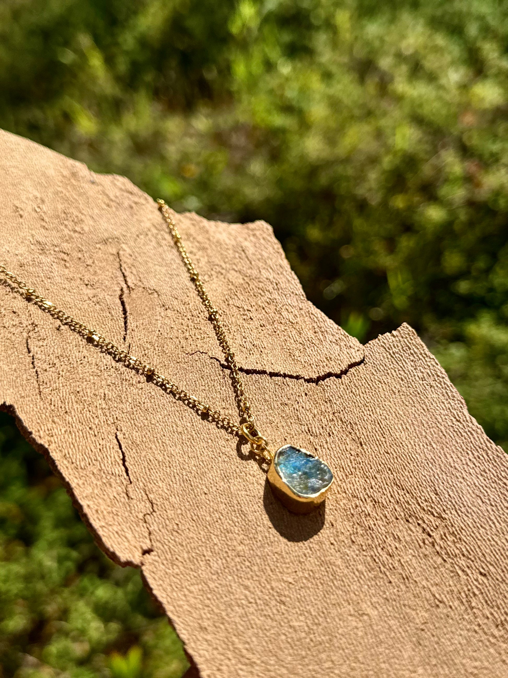 Necklace with a blue pendant on a wooden surface with greenery in the background