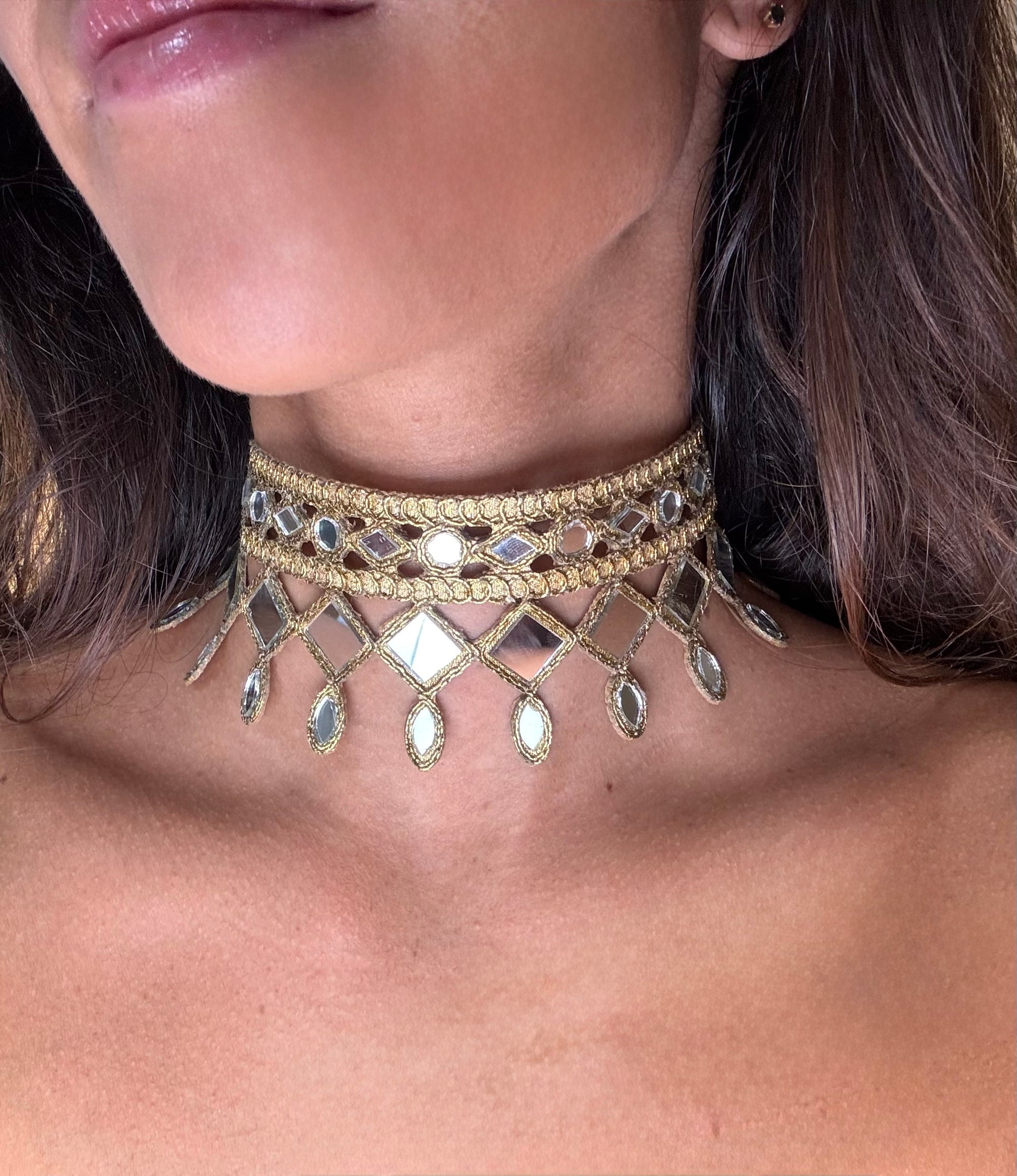 Close-up of a woman wearing a gold choker necklace with reflective stones.