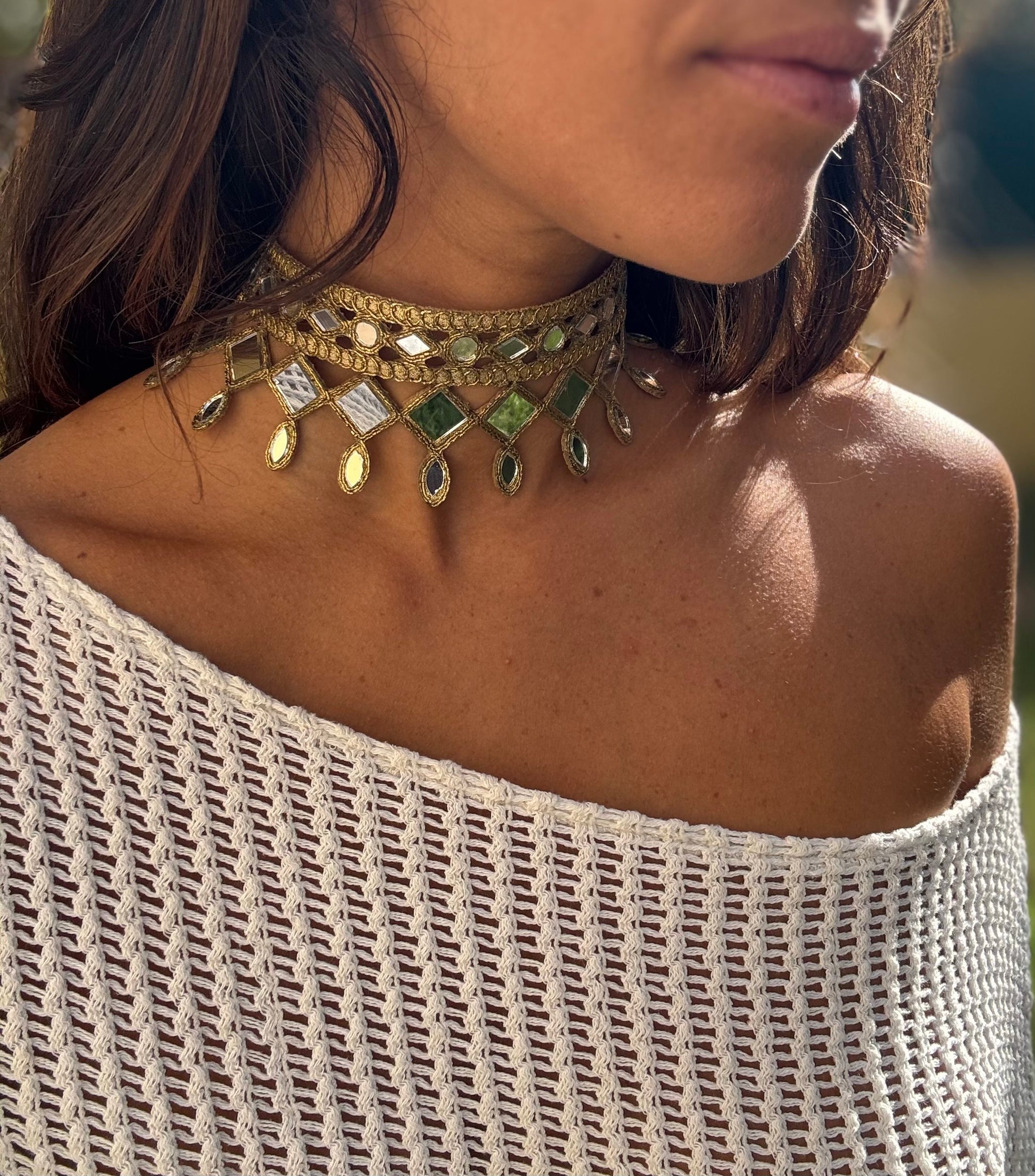 Close-up of a woman wearing a gold and green beaded necklace with a textured off-shoulder top.